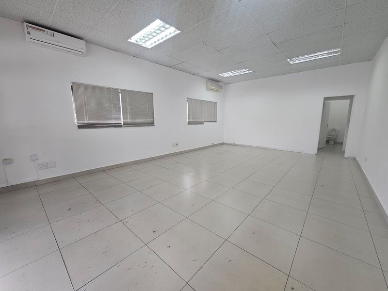 An empty commercial office space featuring tiled flooring, suspended ceilings with recessed lighting, and wall-mounted air conditioning units.