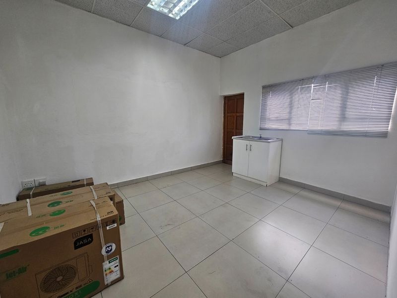 A vacant commercial office space featuring tiled flooring, a drop ceiling, a small kitchenette cabinet with a sink, and venetian blinds.