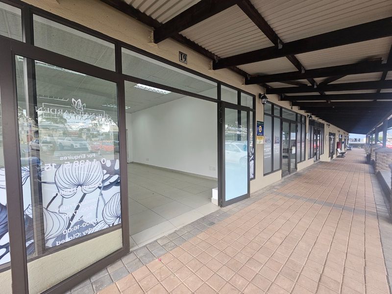 Commercial storefront entrance with aluminum-framed glass doors and a covered tiled walkway in a retail complex.