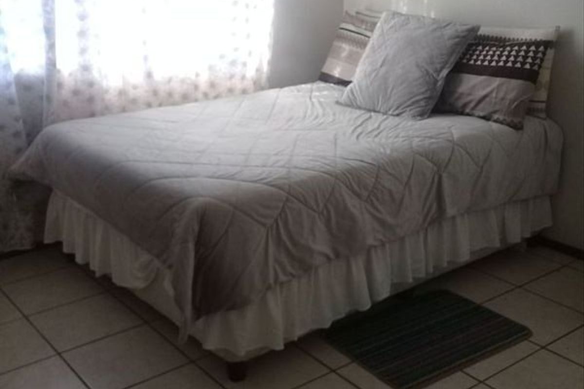 A simple bedroom featuring neutral tiled flooring and a window with sheer curtains.
