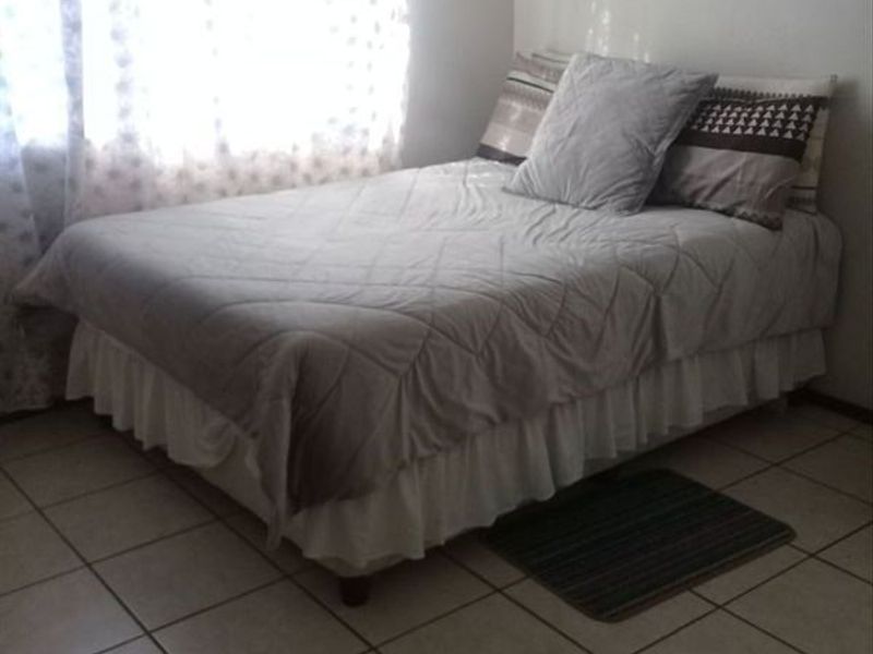 A simple bedroom featuring neutral tiled flooring and a window with sheer curtains.