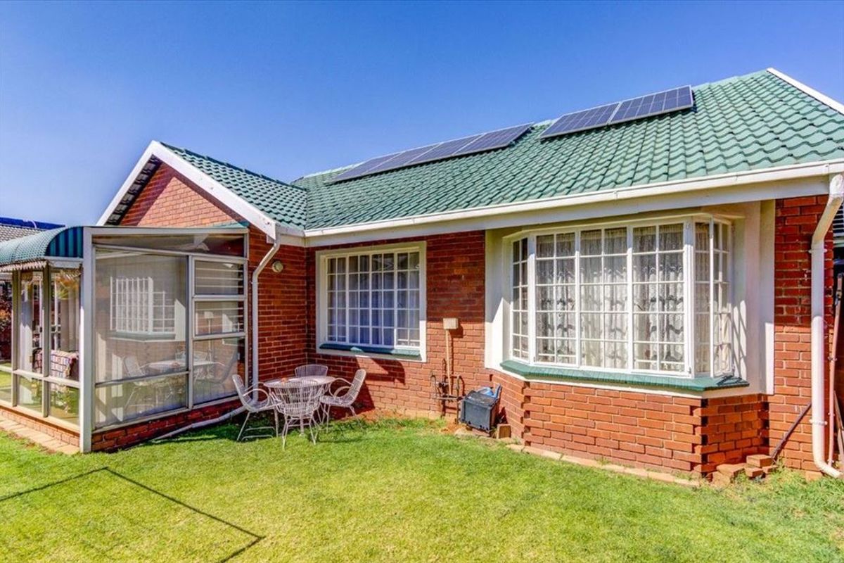 Rear view of the property featuring a brick facade, green tiled roof with solar panels, a bay window, and an enclosed patio area.