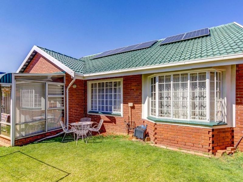 Rear view of the property featuring a brick facade, green tiled roof with solar panels, a bay window, and an enclosed patio area.