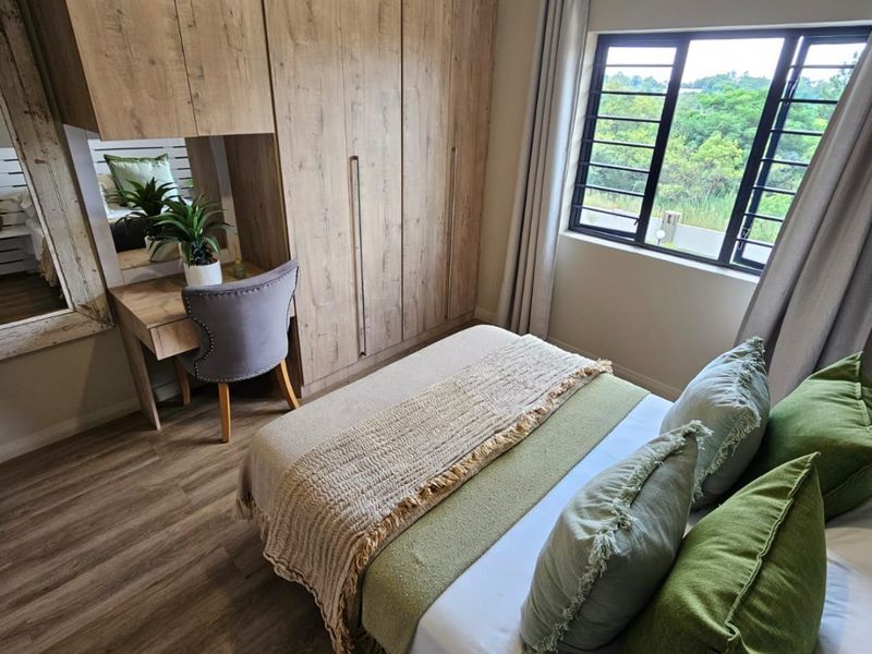 A well-maintained bedroom featuring modern wood-look built-in cupboards, a matching integrated vanity, laminate flooring, and large windows with natural light.