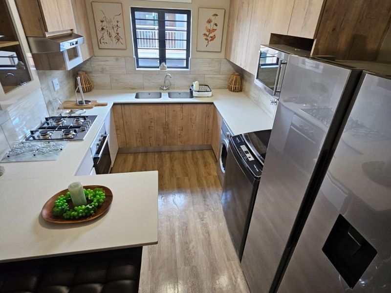 Modern U-shaped kitchen featuring wood-look cabinetry, laminate countertops, integrated gas hob, built-in oven, and durable laminate flooring with a functional layout.