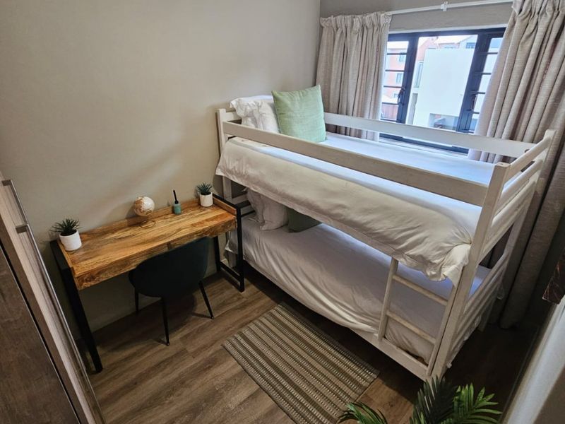 A compact bedroom featuring laminate flooring, neutral wall tones, and a functional window with curtain tracks.