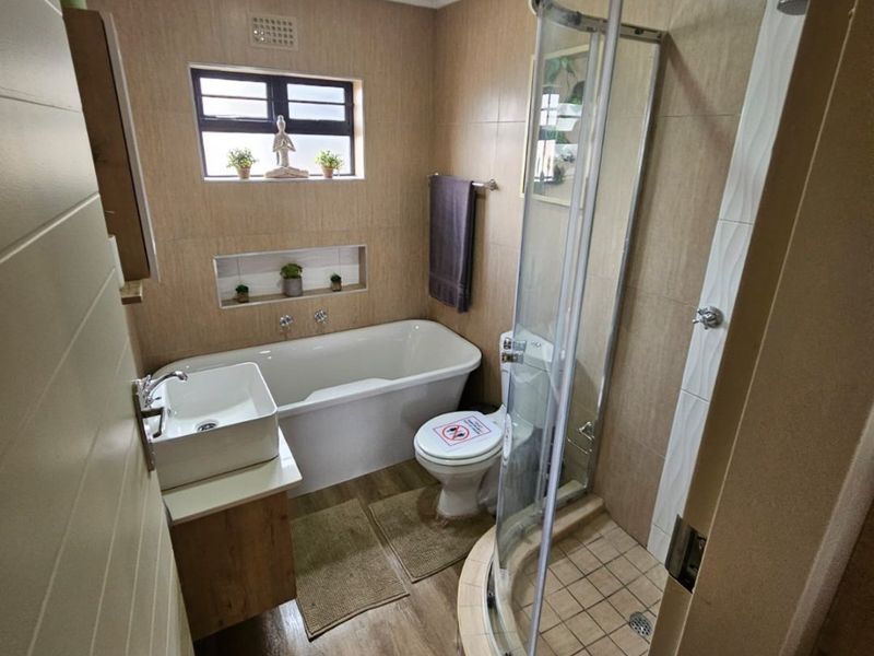 Modern bathroom featuring a separate bathtub and curved glass shower enclosure, vanity with vessel sink, and neutral tiled finishes.
