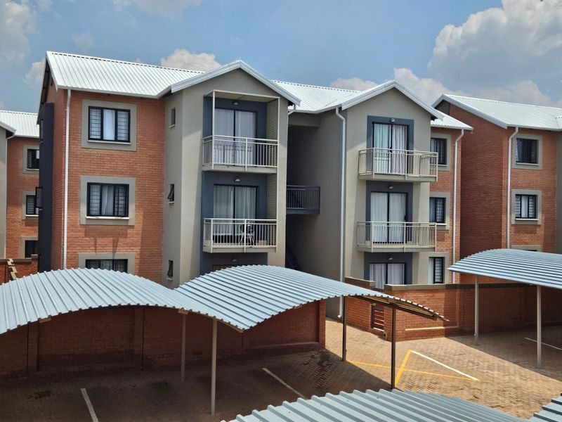 Exterior view of a multi-story apartment complex featuring brick facades, metal roofing, private balconies, and covered carport parking spaces.