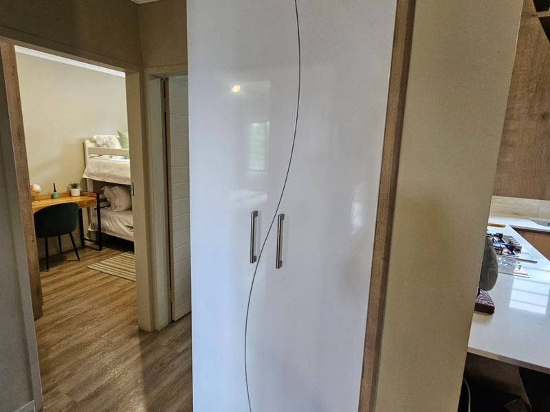 A well-maintained hallway featuring modern laminate flooring and a sleek, white built-in cupboard with a curved design detail.