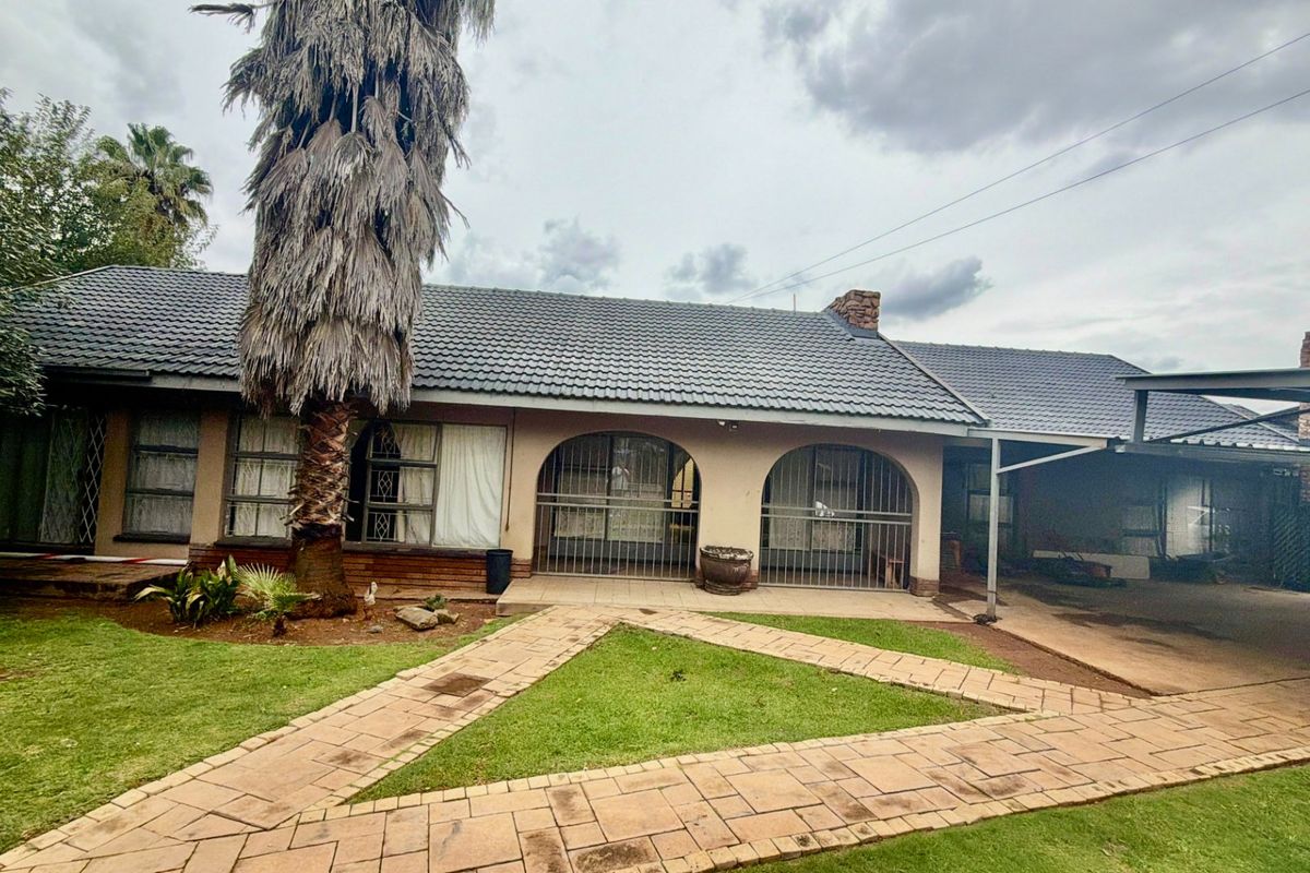 Rear exterior view of the property featuring a tiled roof, paved garden pathways, security-gated arched openings, and an attached carport structure.