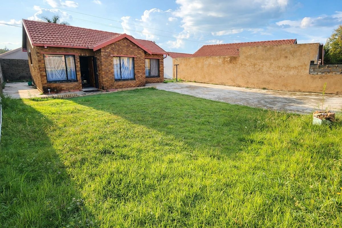 Rear view of a face brick house featuring a tiled roof, concrete driveway, and a spacious backyard with a perimeter boundary wall.