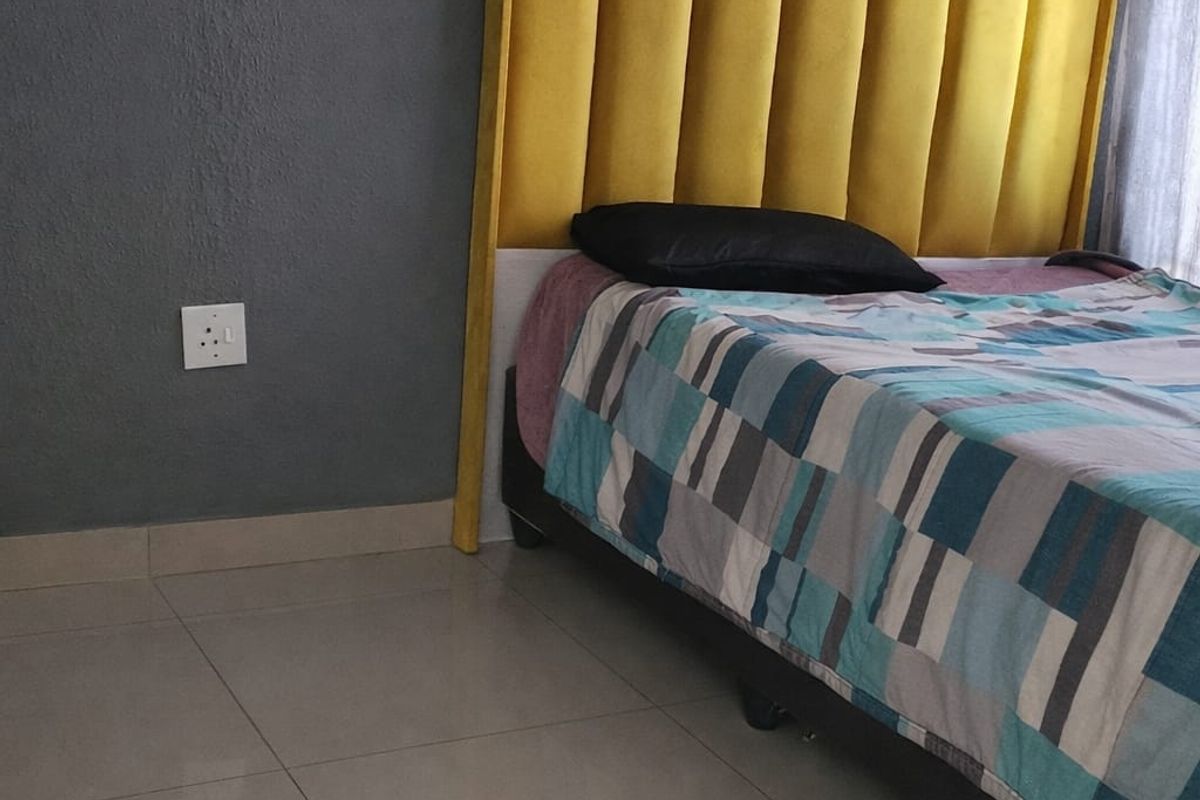 A bedroom featuring neutral tiled flooring and a grey accent wall with an electrical outlet.