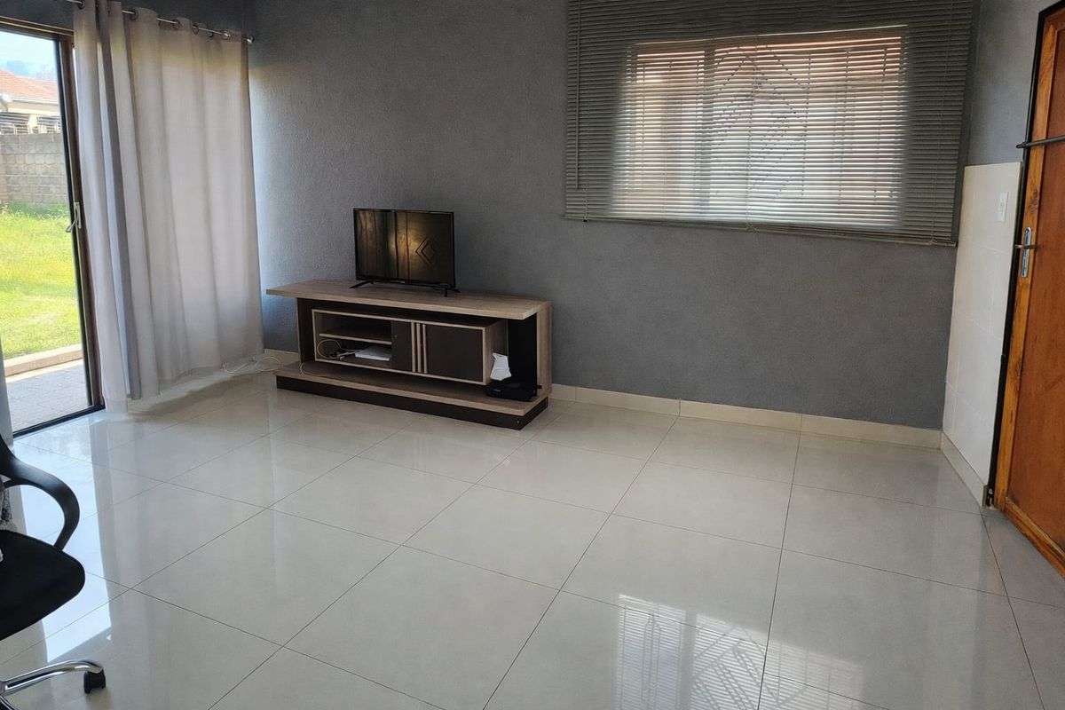 A bright, open living room featuring large format floor tiles, a sliding glass door leading to the garden, and neutral grey wall finishes.