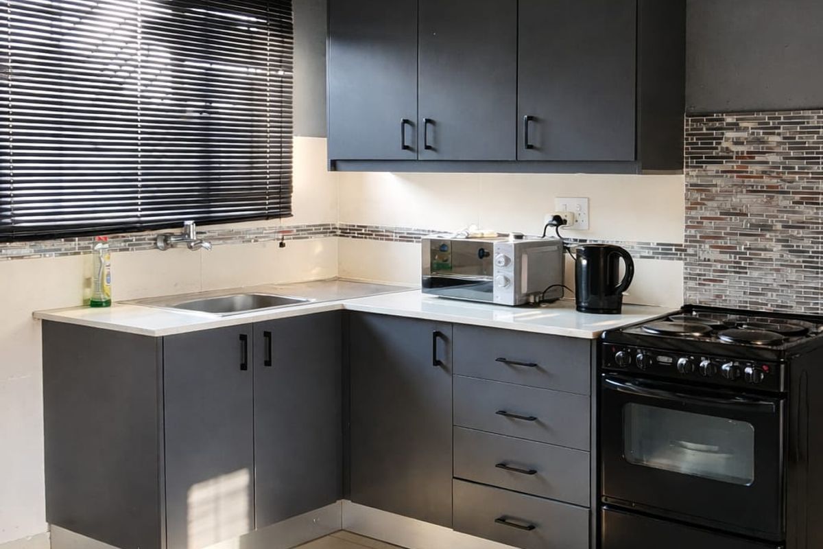A modern kitchen featuring dark grey cabinetry, contrasting white countertops, mosaic tile backsplash, and a freestanding oven, complemented by tiled flooring and natural light.