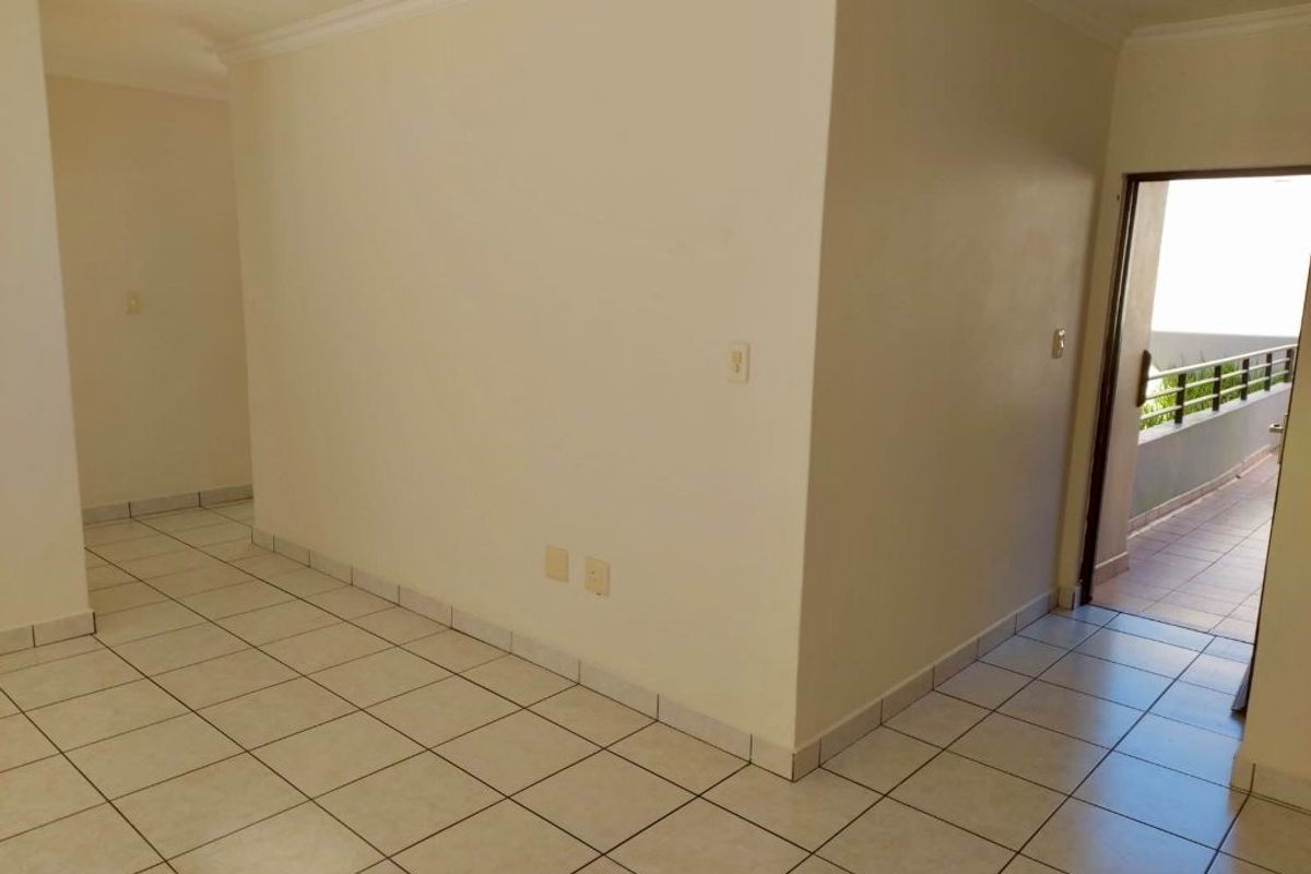An empty, neutral-toned living area featuring ceramic floor tiles, cove cornicing, and direct access to an outdoor balcony space.