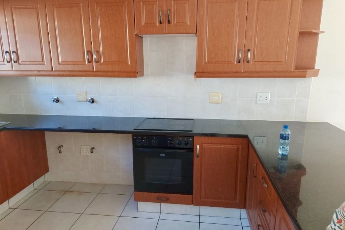 A functional kitchen featuring wooden cabinetry, granite countertops, a built-in oven with hob, and tiled flooring.