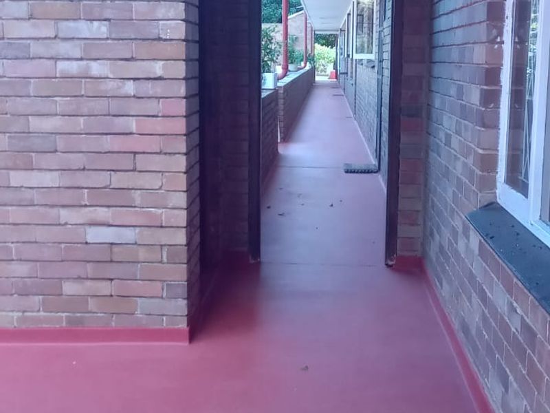 An exterior covered walkway or balcony featuring exposed brick walls and painted concrete flooring, providing access to the townhouse units.