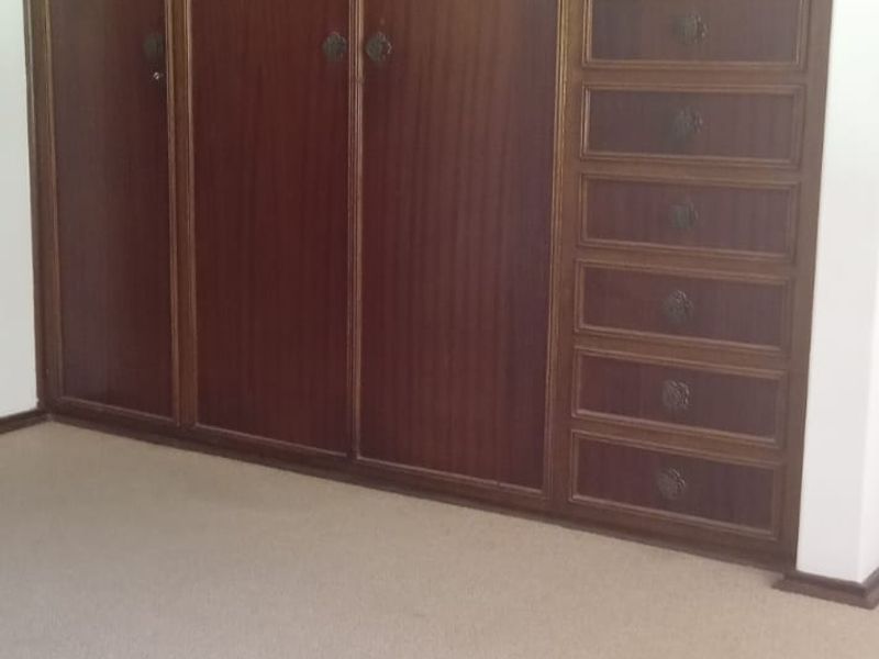 A bedroom featuring extensive floor-to-ceiling built-in wooden cabinetry with integrated drawers and neutral carpeting.
