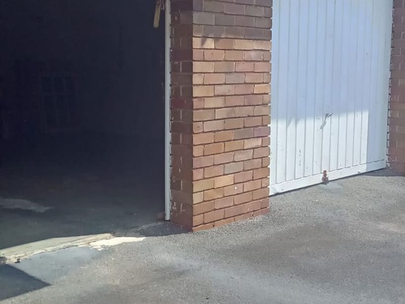 A double garage featuring brick exterior walls, one open bay, and one closed up-and-over door with a concrete driveway.