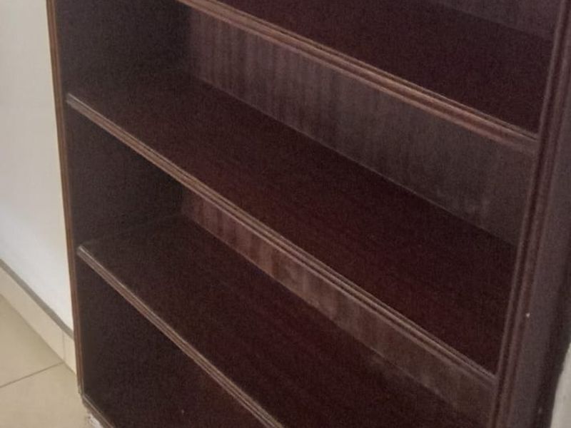 A close-up view of a built-in wooden shelving unit with tiled flooring and visible wear at the base.