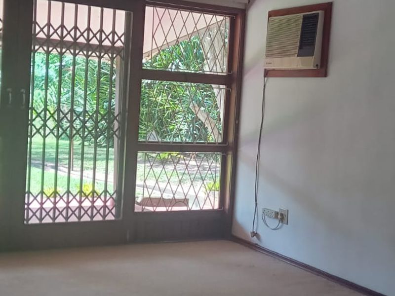 An empty living room featuring a ceiling fan, wall-mounted air conditioner, and sliding glass doors with security gates leading to the garden.