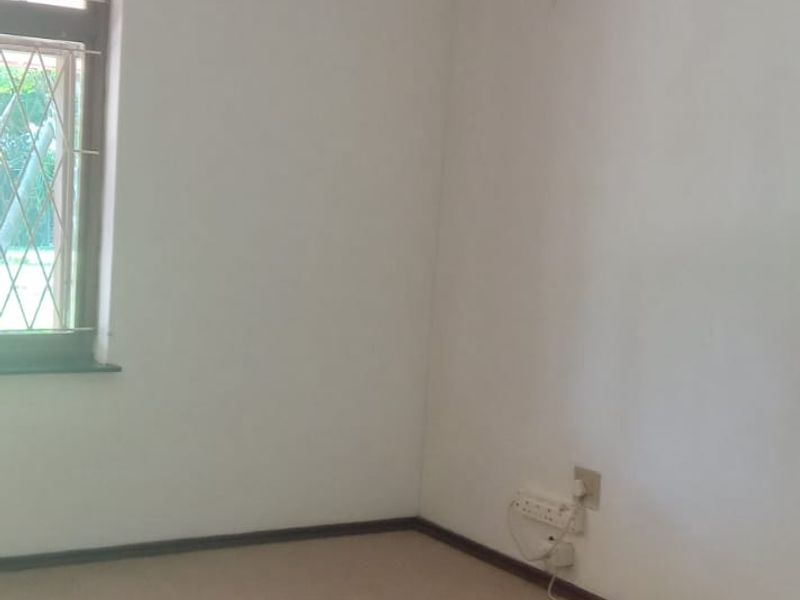 An empty bedroom featuring carpeted flooring, a ceiling fan, and a window fitted with security bars.