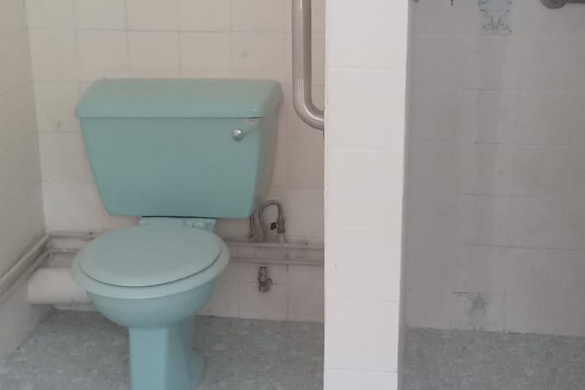 A dated bathroom featuring a light blue toilet, a walk-in shower area with grab rails, and original wall and floor tiling.
