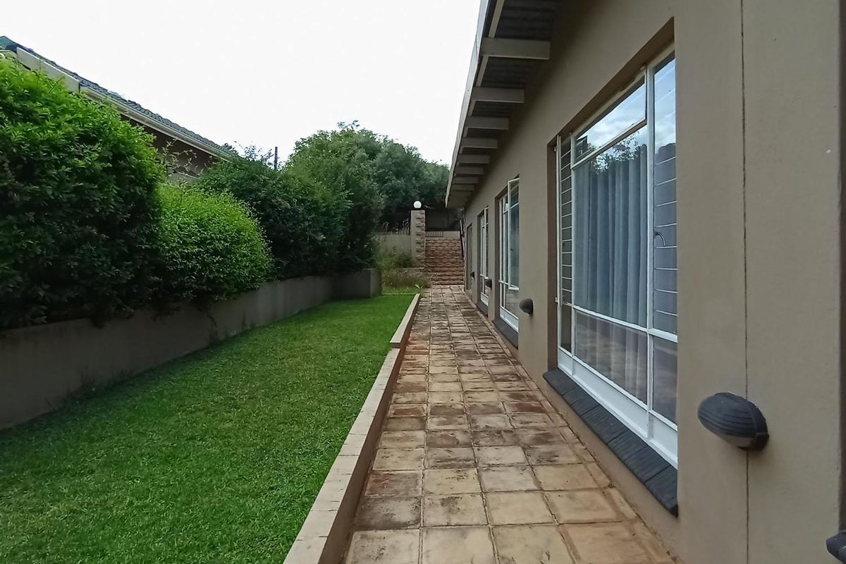A rear exterior view featuring a tiled patio walkway alongside a lawn, retaining wall, and access to the home via sliding glass doors.