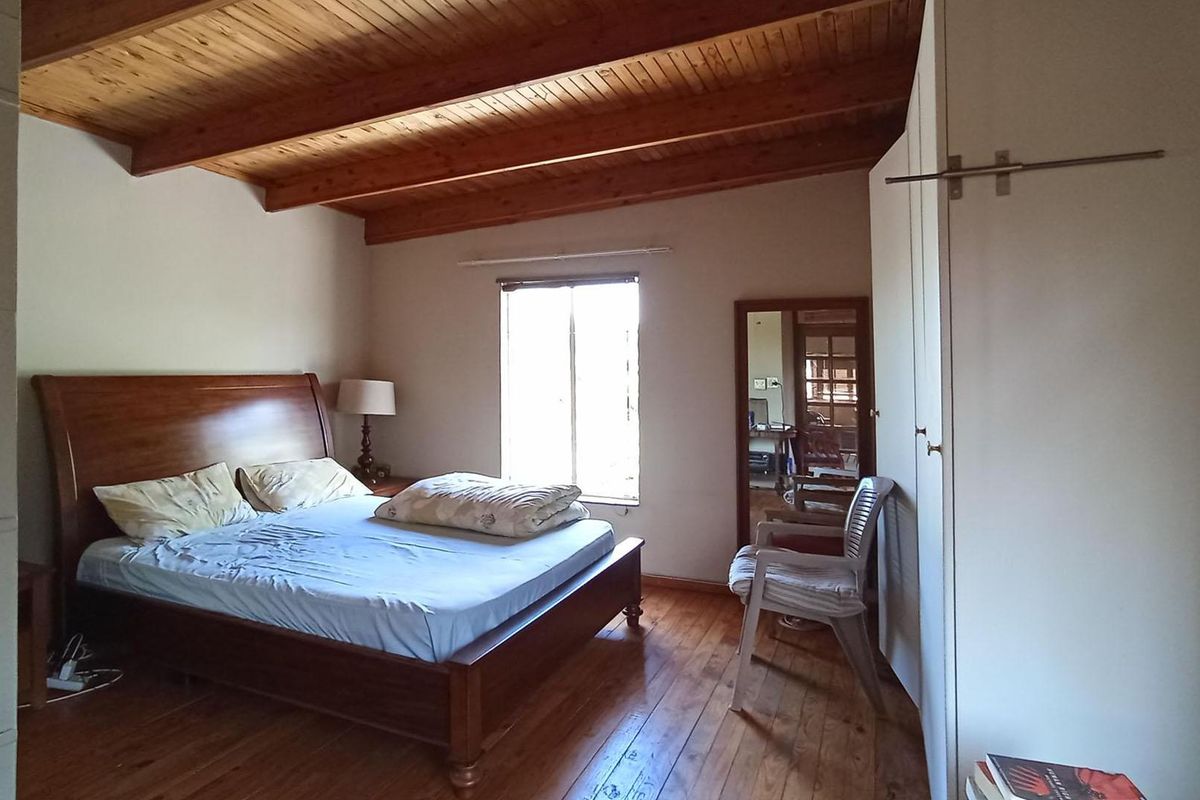 A bedroom featuring exposed timber ceiling beams, polished timber flooring, and built-in storage cupboards.