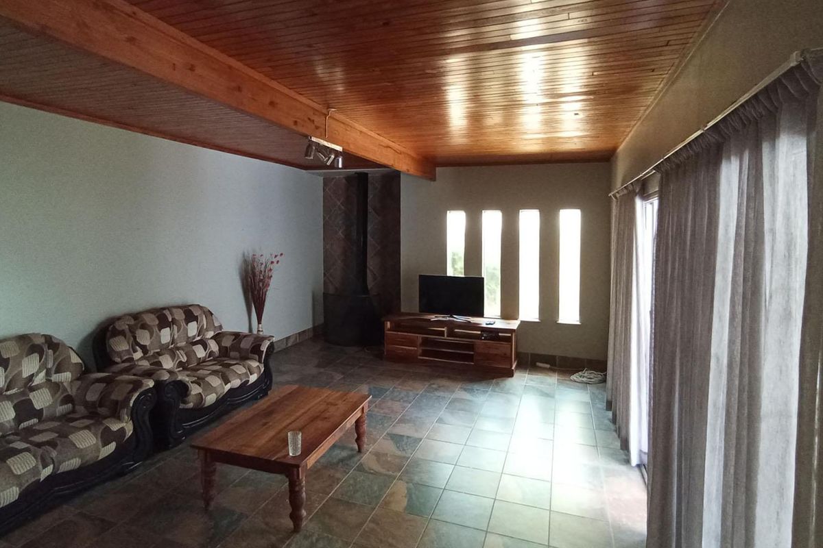 Spacious living room featuring a warm timber-clad ceiling, tiled flooring, and a built-in fireplace, with direct access to the outdoors via sliding glass doors.