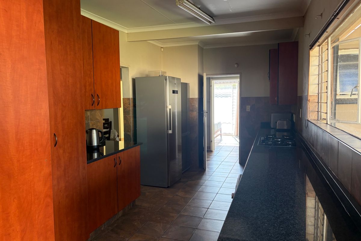 A functional kitchen featuring dark granite countertops, wood-finish cabinetry, gas hob, and tiled flooring with direct access to the exterior.
