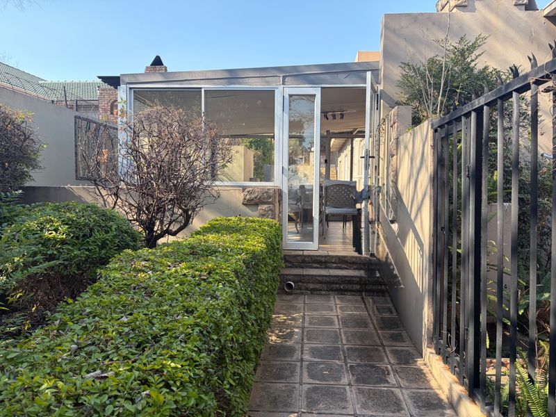 An enclosed patio area featuring sliding glass doors, accessible via a paved walkway and bordered by a landscaped garden and stone retaining wall.