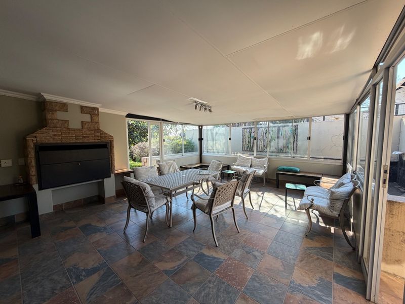 Enclosed patio area featuring a built-in braai with stone detailing, tiled flooring, and large sliding glass doors providing natural light and garden access.