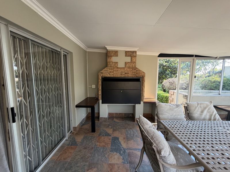 Covered patio area featuring a built-in braai with stone cladding, tiled flooring, and sliding door access to the main house.