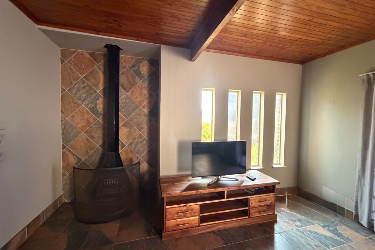 A living room featuring a wood-burning fireplace with a tiled surround, timber-clad ceiling with exposed beam, and tiled flooring.