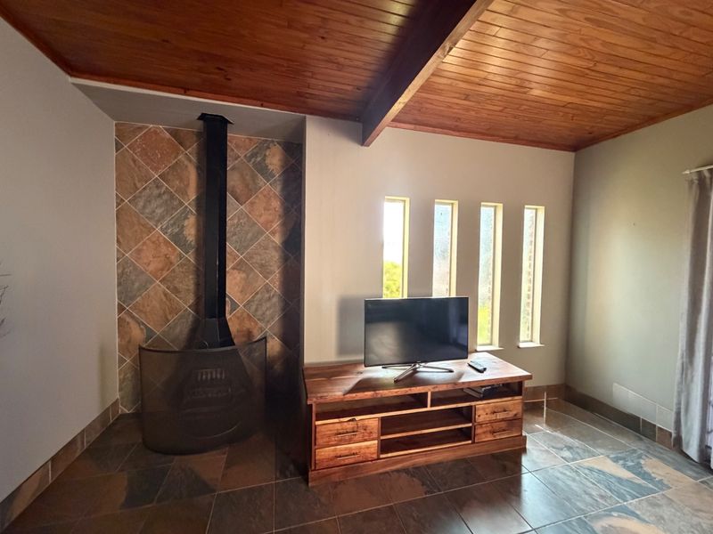A living room featuring a wood-burning fireplace with a tiled surround, timber-clad ceiling with exposed beam, and tiled flooring.