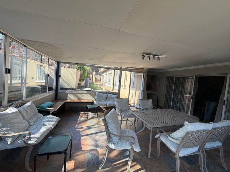 Enclosed patio area featuring tiled flooring, built-in braai, and large glass windows, providing a versatile space for outdoor entertaining.