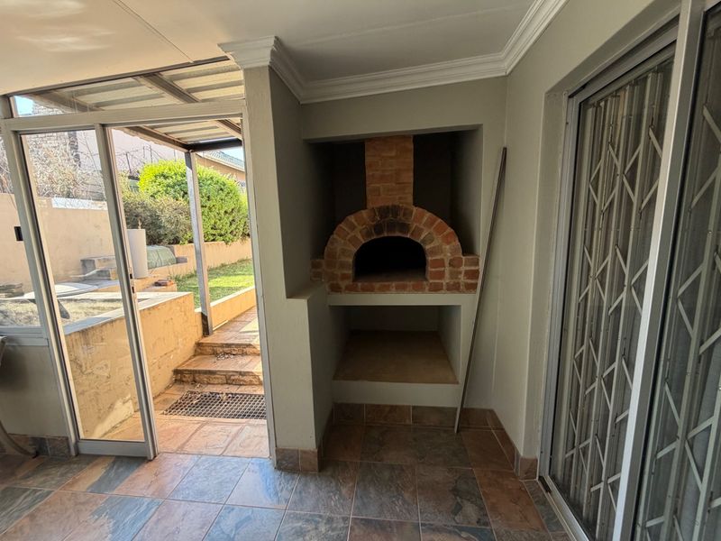Covered patio area featuring a built-in brick pizza oven, tiled flooring, and direct access to the rear garden through sliding glass doors.