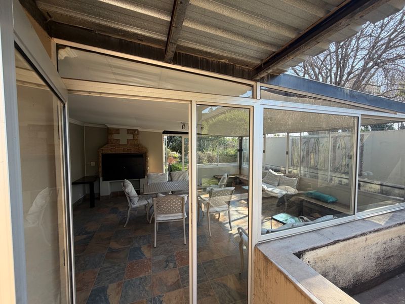 Enclosed patio area featuring slate tile flooring, a built-in brick braai, and large aluminium sliding doors providing access to the garden.