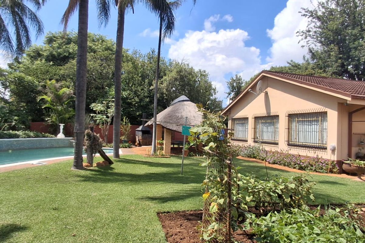 Spacious rear garden featuring a swimming pool, a thatched lapa with a built-in braai, and well-maintained lawn areas.