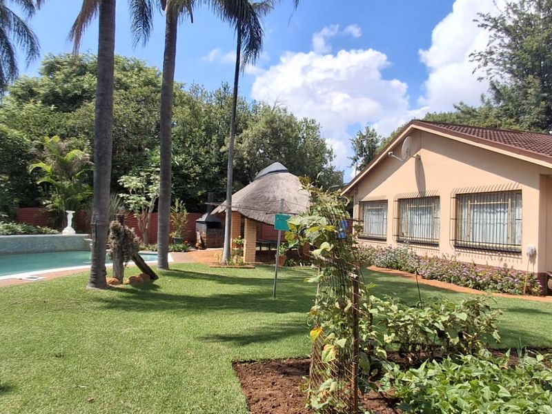 Spacious rear garden featuring a swimming pool, a thatched lapa with a built-in braai, and well-maintained lawn areas.