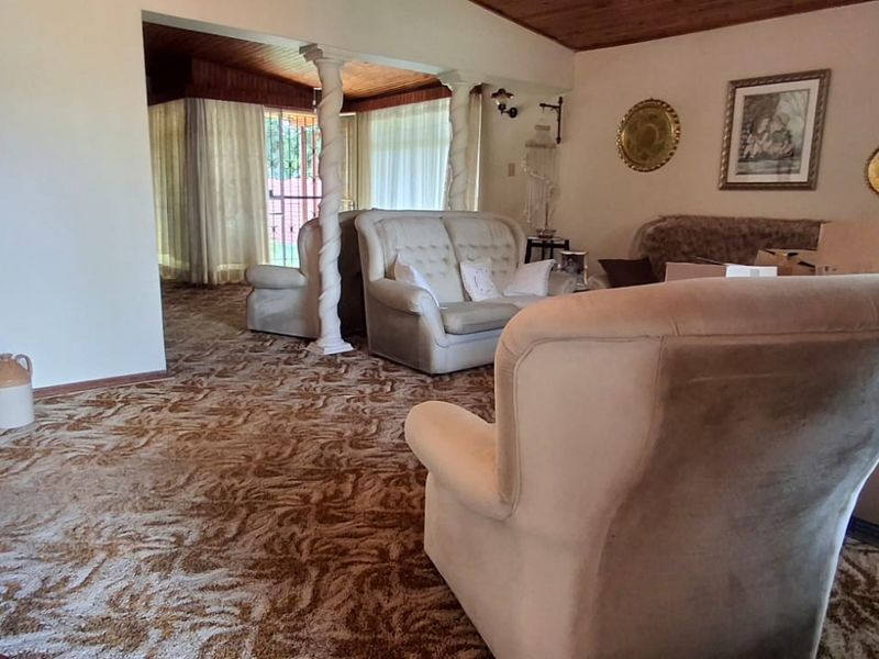 Spacious living area featuring a timber-paneled ceiling, decorative columns, and wall-to-wall carpeting, offering a traditional layout with potential for modernization.