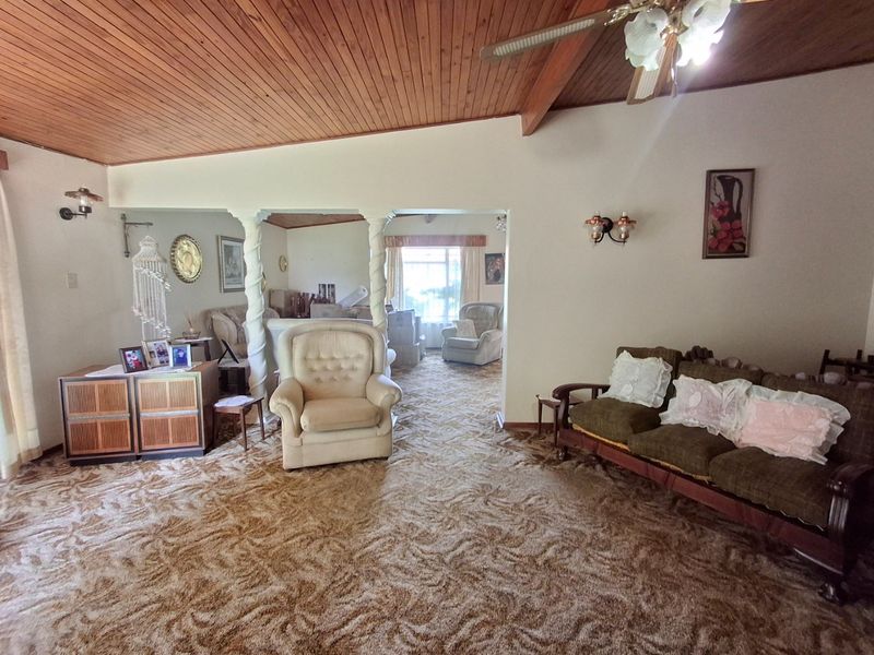 Spacious open-plan living area featuring a vaulted timber-clad ceiling, decorative columns, and wall-mounted lighting, offering a dated aesthetic ready for modernization.