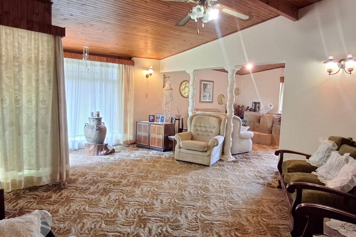 Spacious living area featuring a timber-clad ceiling, decorative columns, and wall-mounted lighting, offering a dated aesthetic ready for modern updates.