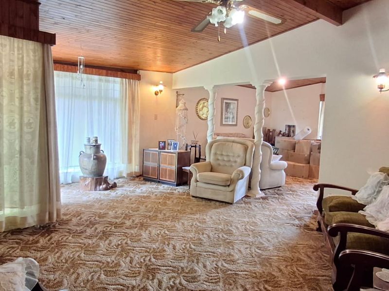 Spacious living area featuring a timber-clad ceiling, decorative columns, and wall-mounted lighting, offering a dated aesthetic ready for modern updates.