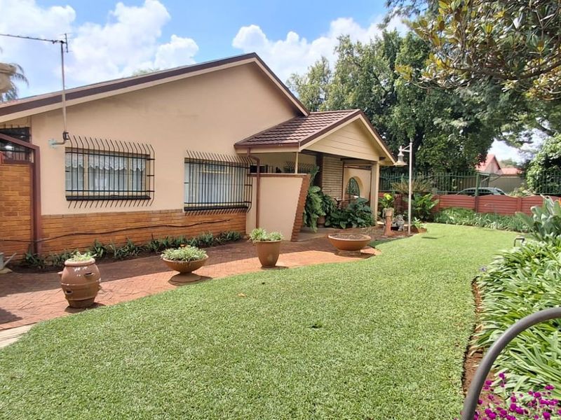 A well-maintained rear exterior view featuring a landscaped garden, paved walkway, and a covered patio area with classic architectural columns.