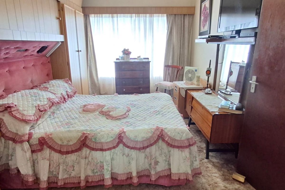 A dated bedroom featuring built-in wooden cupboards, wood paneling, and a large window with curtains, offering a blank canvas for modernization.