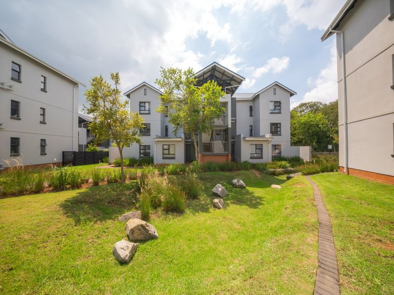 A view of the townhouse complex exterior featuring well-maintained landscaped gardens, paved pathways, and modern multi-story residential buildings.