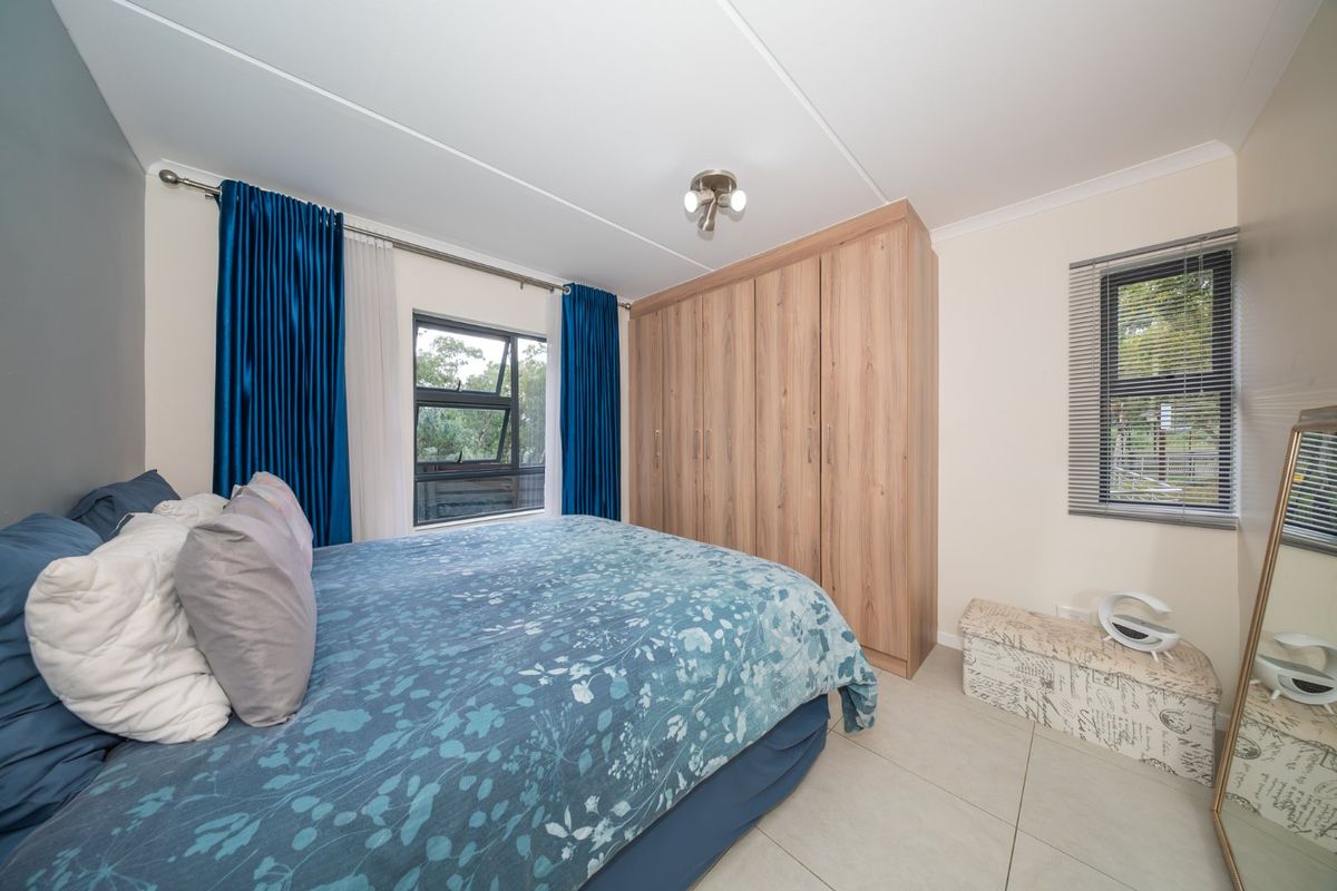 A well-maintained bedroom featuring neutral tiled flooring, built-in wooden wardrobes, and aluminium-framed windows providing natural light.