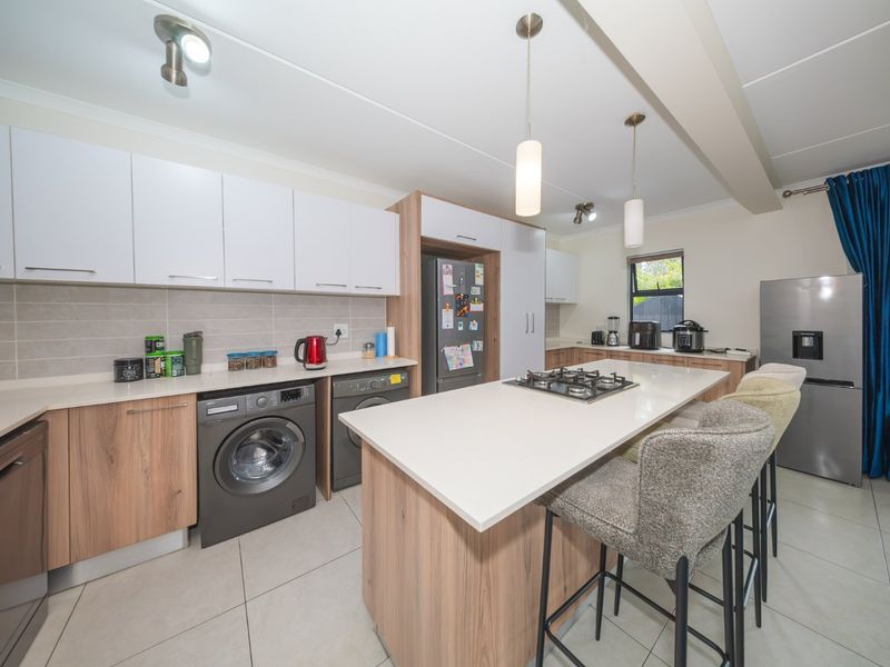 Modern kitchen featuring light wood-tone cabinetry, white stone countertops, a central island with a gas hob, and integrated laundry facilities.
